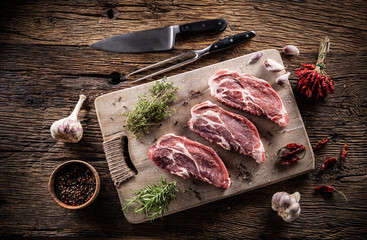 Wall Mural - Three sliced pieces of pork neck with herbs, chili spices and garlic on a cutting board