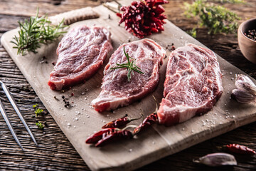 Wall Mural - Three sliced pieces of pork neck with herbs, chili spices and garlic on a cutting board.