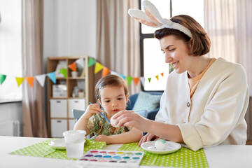 Poster - holidays, family and people concept - happy mother and little baby daughter coloring easter eggs with watercolors at home