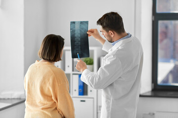 Wall Mural - medicine, healthcare and people concept - male doctor showing x-ray to female patient at medical office in hospital