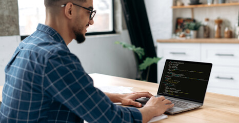 Panoramic side view photo of a programmer with laptop. Clever successful guy, an IT specialist, software developer, uses laptop, male programmer prescribes codes for an application. IT technology