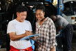 © feeling lucky - Man technician car mechanical in half uniform show car maintenance service report on clipboard at repair garage station. Auto mechanic give customer discussion on her vehicle repair problems condition