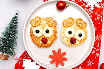 Christmas deers face shaped pancake with sweet fresh raspberry berry and cheese on plate for kids baby children breakfast dinner. xmas food with new year decorations on gray background close up