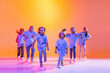 Group of children, little girls in sportive casual style clothes dancing in choreography class isolated on orange background in purple neon light.