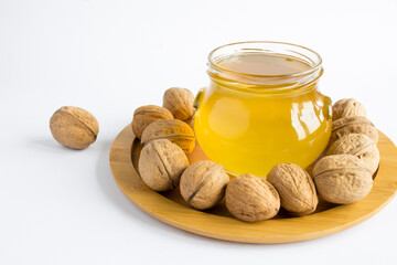 Wall Mural - Honey in the glass jar and walnuts on the white background. Close-up.