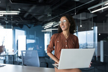 Portrait Young Beautiful Woman With Curly Hair, Successful Woman In Glasses Smiling And Looking Out Window, Business Woman Freelancer Working In Office Standing With Laptop Smiling Looking Out Window