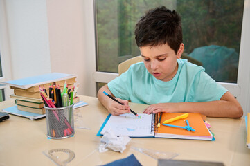 Confident smart student, schoolboy using a colored pencil, draws and calculates the surface of geometric shapes, doing geometry homework. The concept of returning to school in the new academic year
