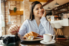 Smiling Woman Sitting At Table And Having Breakfast In Cafe With Photo Camera.