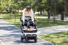 Lifestyle Young Casual Caucasian Mother With Two Little Twin Girls In A Double Baby Stroller Walks In City The Park 