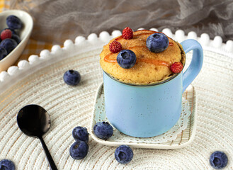 Delicious homemade blueberry muffin mug cake with fresh berries . Cooked in a cup in the microwave. cupcake in a blue mug decorated with blueberries. vanilla mugcake dessert. Easy to cook concept