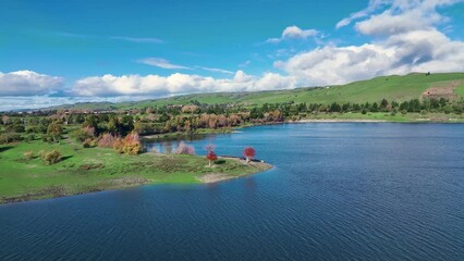 Poster - Drone view of small city with beautiful view of lake, green hills in natural place under blue sky.