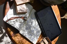 Round Table With A Notebook, Glasses, And A Tablet With Drawing Drafts Under Sunlight