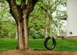 Beautiful view of a swing from tire and rope on a large outside of a white house beside a green area