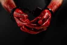 Close-up Of Male Bloody Handcuffed Hands On A Black Background.