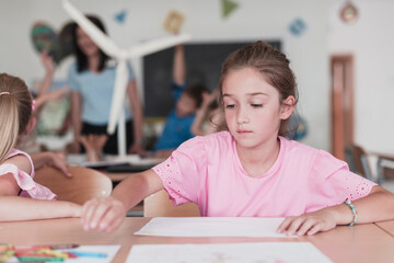 Little girls sitting in elementary school drawing on paper with their friends while sitting in a modern classroom