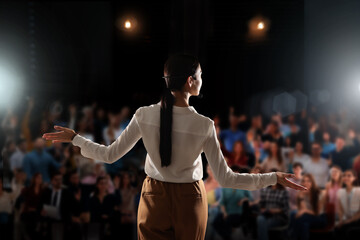 Motivational speaker with headset performing on stage, back view