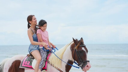 Wall Mural - Asian young mother and daughter horseback riding on the beach together	
