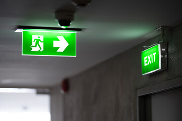a green fire exit sign is placed on the ceiling along the dimly lit corridor and there is green exit