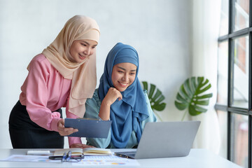 Wall Mural - Two beautiful Muslim Asian businesswomen wearing hijab We are discussing work in various field there is an exchange of idea. and exchanging knowledge by using a laptop computer to work.