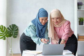 Wall Mural - Two beautiful Muslim Asian businesswomen wearing hijab We are discussing work in various field there is an exchange of idea. and exchanging knowledge by using a laptop computer to work.