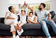 © Allistair F/peopleimages.com - Happy parents and excited children celebrate on the sofa while watching tv. Fun family time, relaxing at home and bonding. Mother and father high five, kids cheer for sports team win.