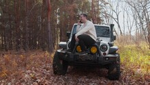 Young Man In White Sweater Sits On His White Car And Talks On Phone In Autumn Forest
