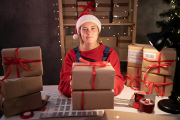 Happy girl Santa Claus packing present box wrapping gift preparing post shipping delivery parcel on table in workshop at night. Merry Christmas shipping delivery