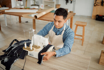 Creative fashion designer or seamstress tailor working on sewing trendy and stylish clothing garment in design studio workshop. Young male dressmaker working on fabric material with machine stitch