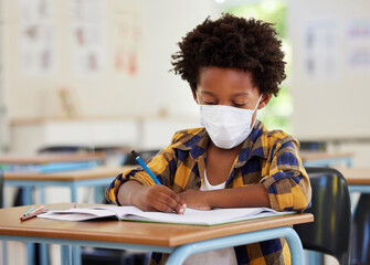 Wall Mural - School boy, student and learning while writing and working in his book inside a classroom with a mask due to covid. Young, serious and African child drawing on paper. Smart kid getting an education