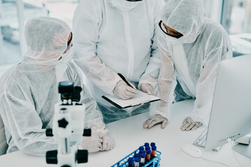 Poster - Team of scientists, pathologists and doctors in hazmat suits discussing forensic research and plans in a lab. Medical experts working on tests, experiments and drug trial to develop cure for disease