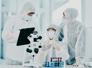 Canvas Print - Science and medical research doctors working on covid vaccine test while wearing protective hazmat suits in modern medicine laboratory. Group of healthcare scientists discussing blood treatment