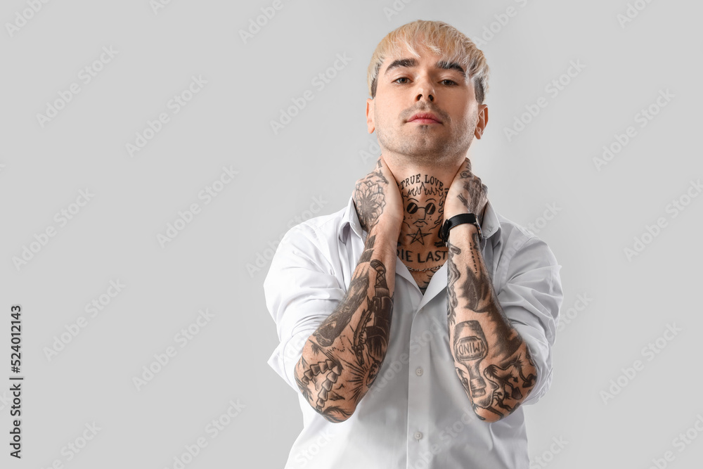 Young tattooed man in white shirt on light background