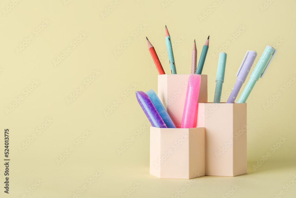 Cups with pens, pencils and glitters on beige background