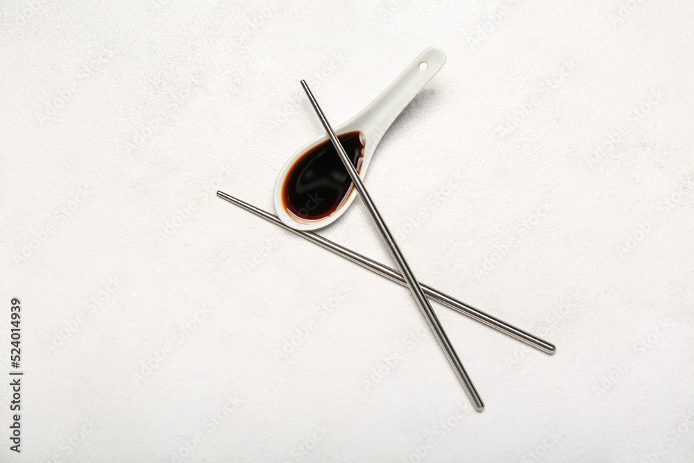 Spoon of soy sauce and chopsticks on white background