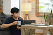 © Prathankarnpap - Casual asian male drinking coffee and reading online news on his laptop while sitting in cozy living room