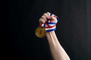 Wall Mural - Human hand holding gold medal on black background