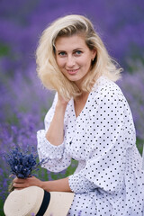 Wall Mural - Romantic young woman in a white dress and straw hat in a lavender field on the sunset	