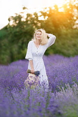 Wall Mural - Romantic young woman in a white dress and straw hat  in a lavender field on the sunset  