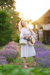 Wall Mural - Romantic young woman in a white dress and straw hat in a lavender field on the sunset	