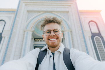 Happy caucasian male traveler takes selfie photo against white mosque of NurSultan Astana Kazakhstan city center