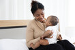 © offsuperphoto - close up African young mother carrying and playing with her adorable baby on bed