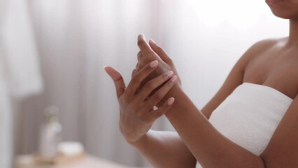 Wall Mural - After shower body care. Unrecognizable african american woman wrapped in towel rubbing pampering lotion on hand