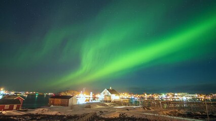 Wall Mural - Beautiful aurora borealis, Northern lights over illuminated fishing village on arctic ocean coastline at Lofoten Islands, Norway