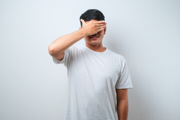 Wall Mural - Young handsome asian man wearing casual shirt standing over covering one eye with hand, confident smile on face and surprise emotion.