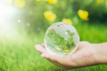 Human hands holding earth sphere crystal or sustainable globe glass with sunlight at green nature background in ecology environment forest. concept of conservation environmental, protection planet.