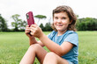 © ADDICTIVE STOCK - Cheerful girl using smartphone on park lawn