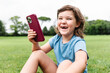 © ADDICTIVE STOCK - Cheerful girl using smartphone on park lawn
