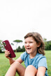 © ADDICTIVE STOCK - Cheerful girl using smartphone on park lawn