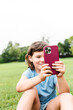 © ADDICTIVE STOCK - Cheerful girl using smartphone on park lawn