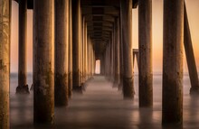 Landscape Of Pier With Columns On Huntington Beach At Golden Sunset With Steam Rising From The Water